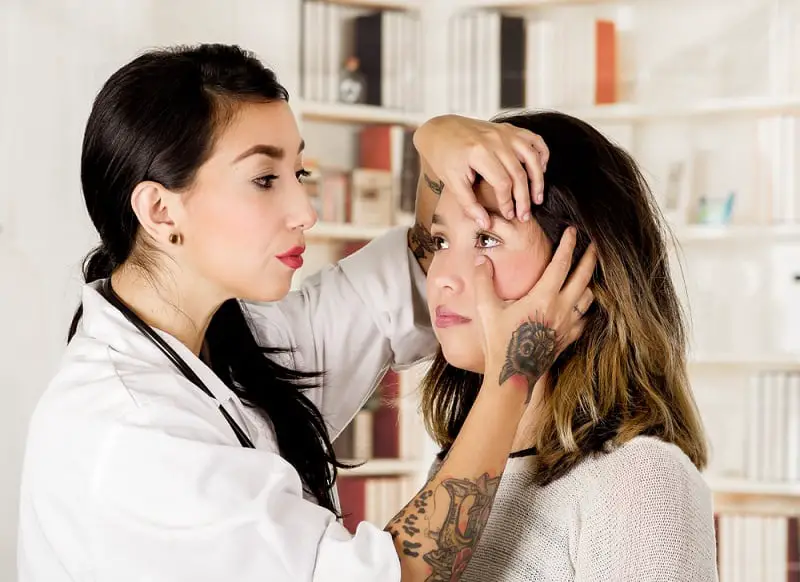 Beautiful tattooed young doctor using her hand to check the eyes of her patient